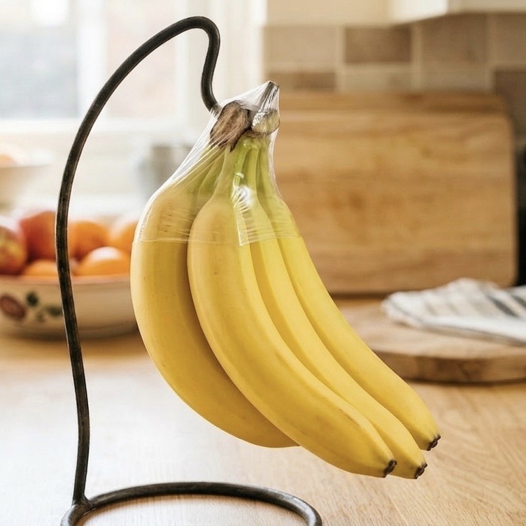 A bunch of yellow bananas hanging on a banana hanger stand on a bright kitchen counter next to a window
