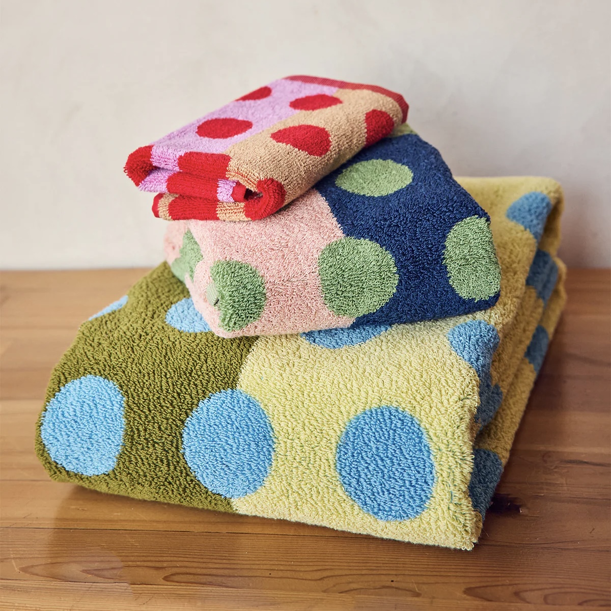 Stack of colorful polka dot towels in blue, green, and red from Dusen Dusen on a wooden surface with a neutral background