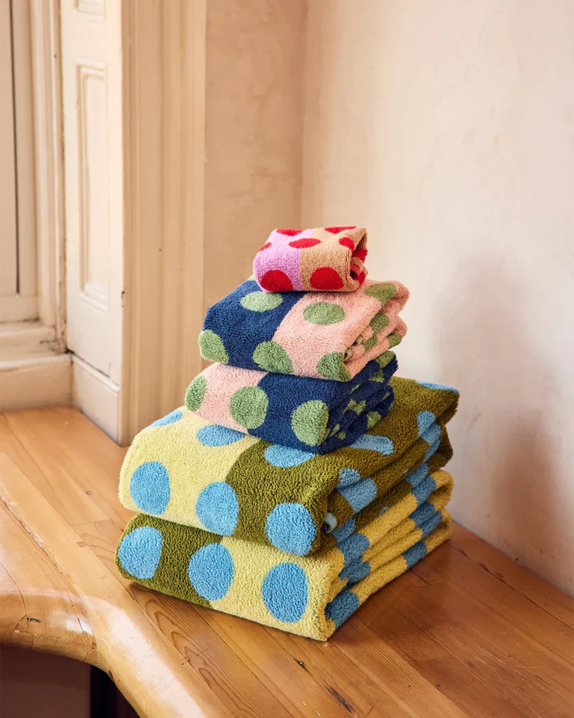 Stack of colorful polka dot towels in blue, green, and red from Dusen Dusen on a wooden surface with a neutral background