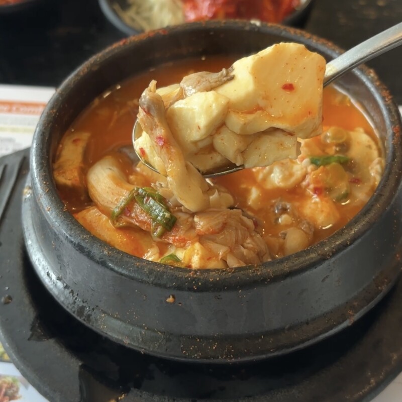 A steaming bowl of BCD Soon Tofu soup with soft tofu and seafood being lifted with a spoon