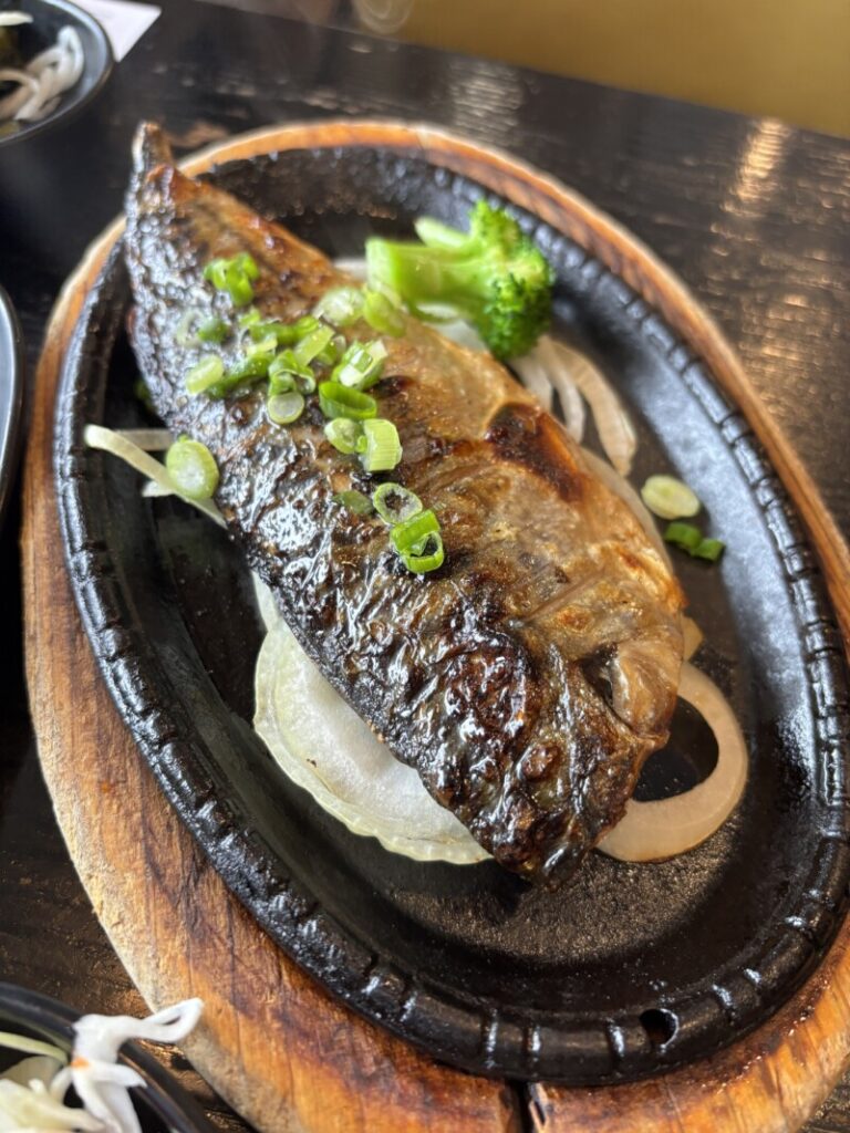 Golden grilled mackerel served on a hot plate with a side of lemon and broccoli
