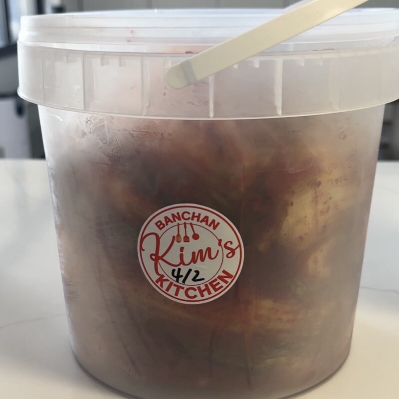A clear plastic bucket of store-bought kimchi from Kim