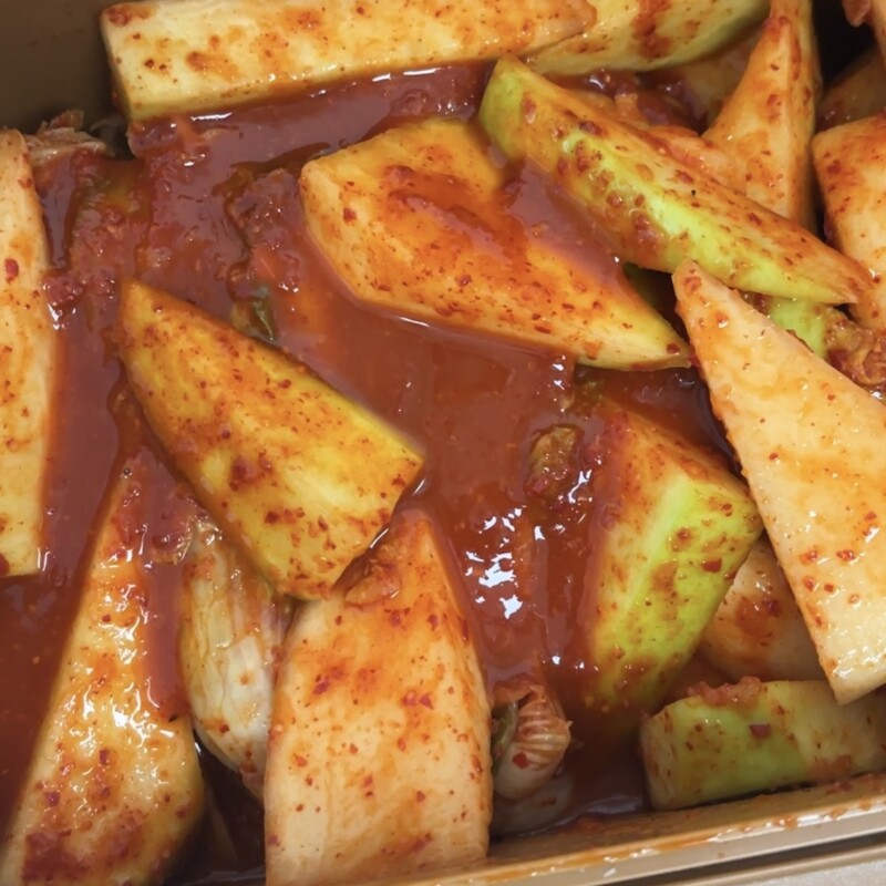 Large slices of sweet Jeju radish mixed with spicy kimchi seasoning in a container