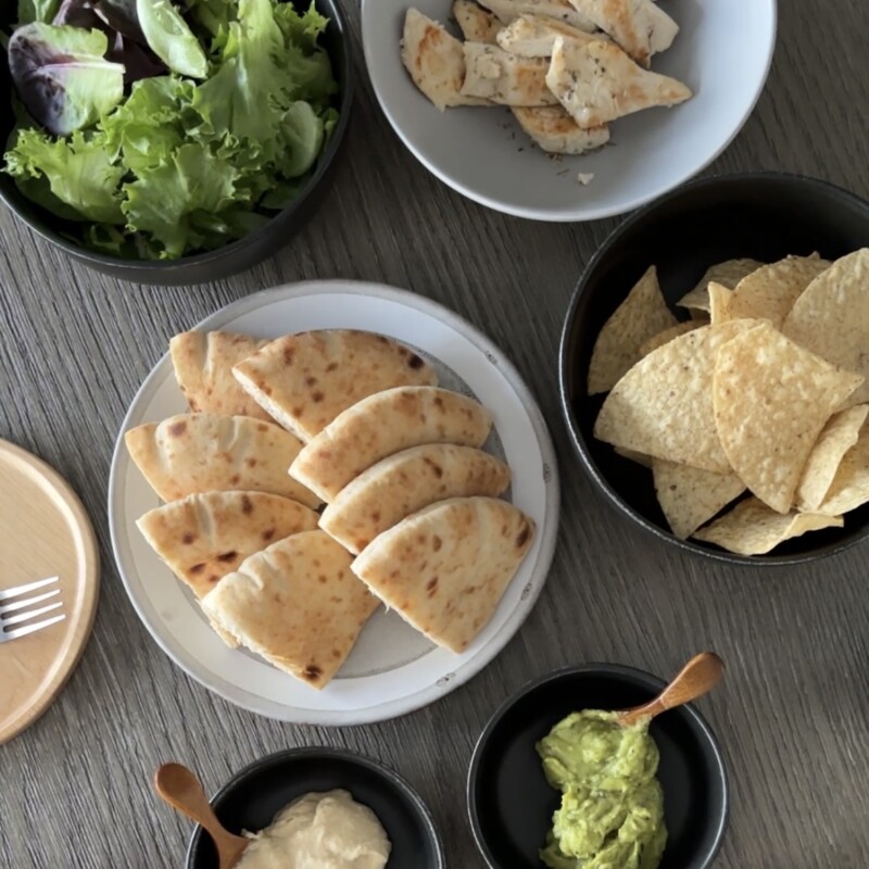 A complete Mediterranean dinner spread with pita wraps, salad, and wine on a modern wooden table