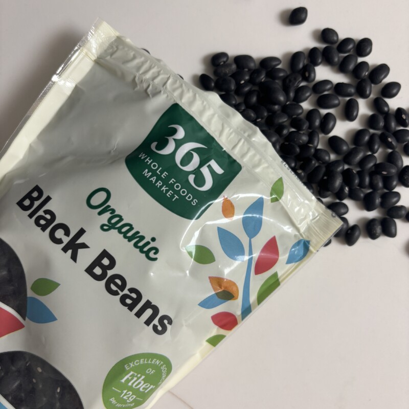 A dark purple morning smoothie made with cooked black soybeans, black sesame, and purple sweet potato, next to a bag of 365 by Whole Foods Market organic black beans